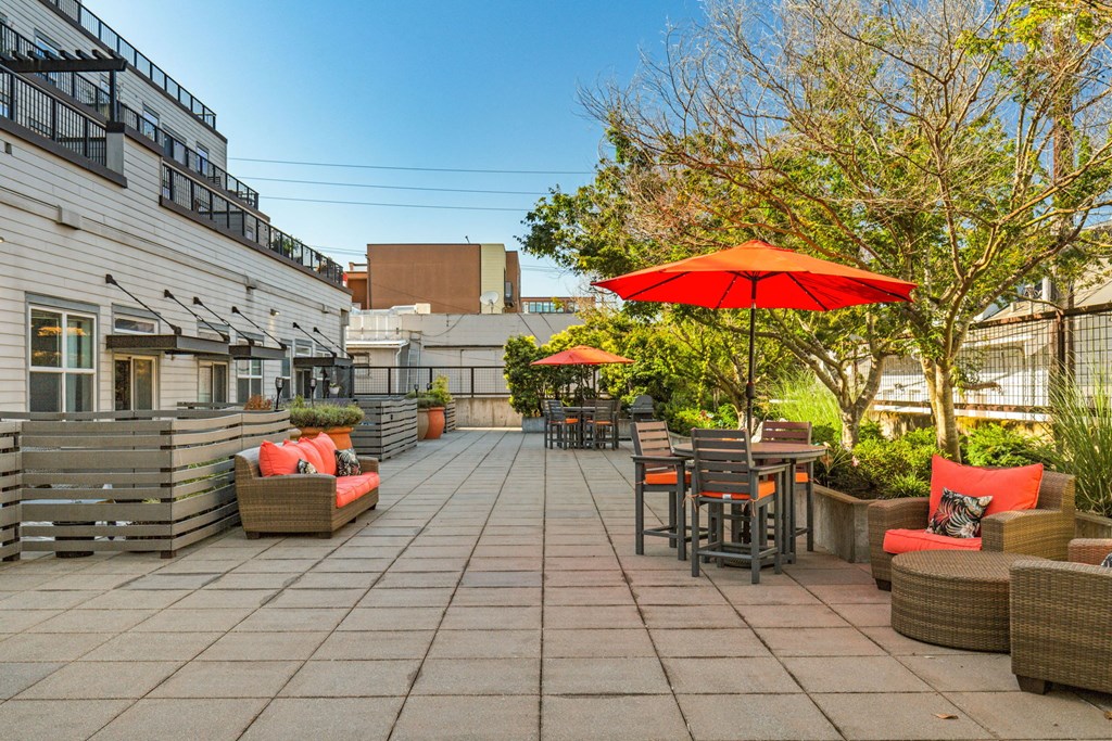 a patio with tables and chairs and a red umbrella