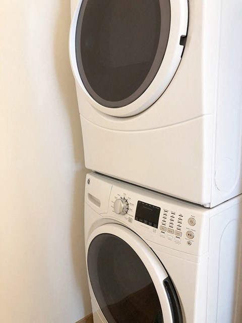 Two white front loading washing machines stacked on top of each other.