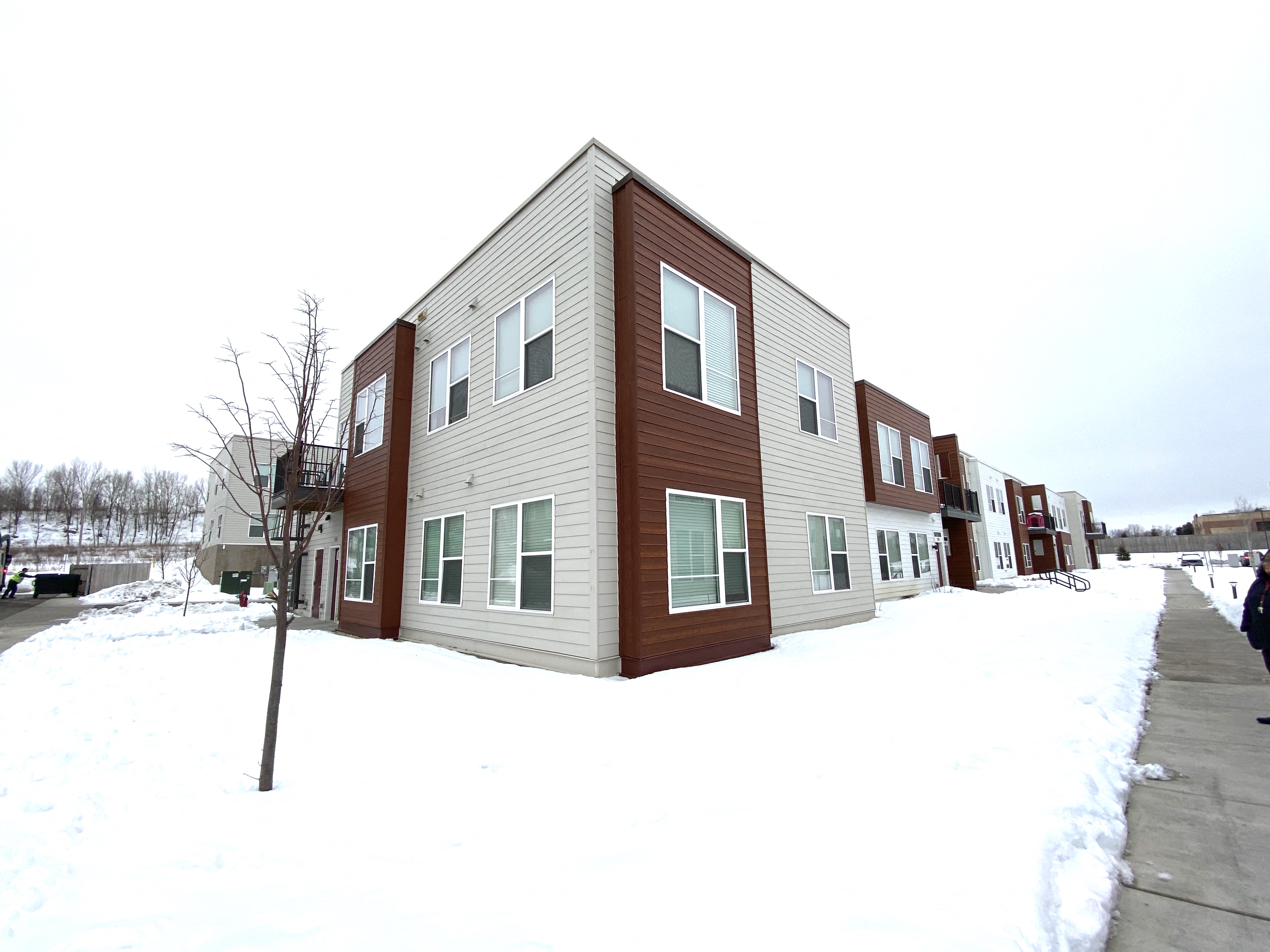 Apartment building with snow on the ground and trees in the background.