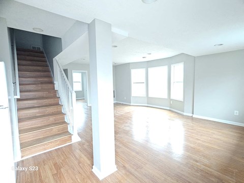 A spacious room with wooden floors and a staircase leading to another level.