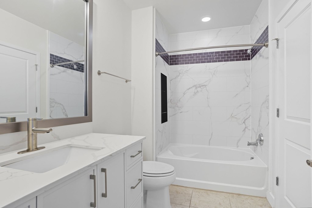 A white bathroom with a marble patterned tub and a toilet.