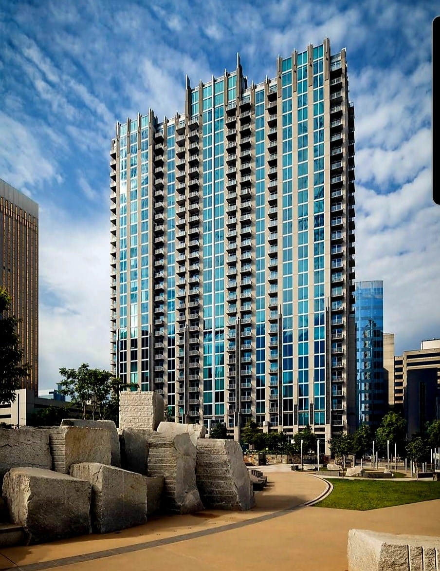 A tall building with blue glass windows stands in front of a sky with clouds.