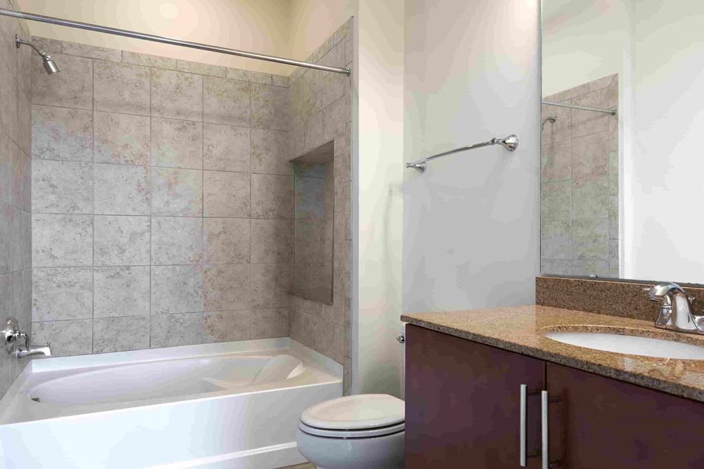 A bathroom with a white bathtub, toilet, and a sink with a brown cabinet.