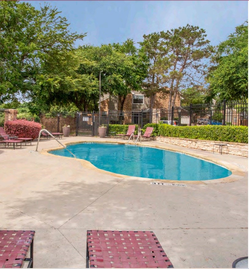 a swimming pool in a park with trees and a fence