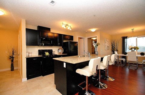 a kitchen with black cabinets and a bar with white chairs