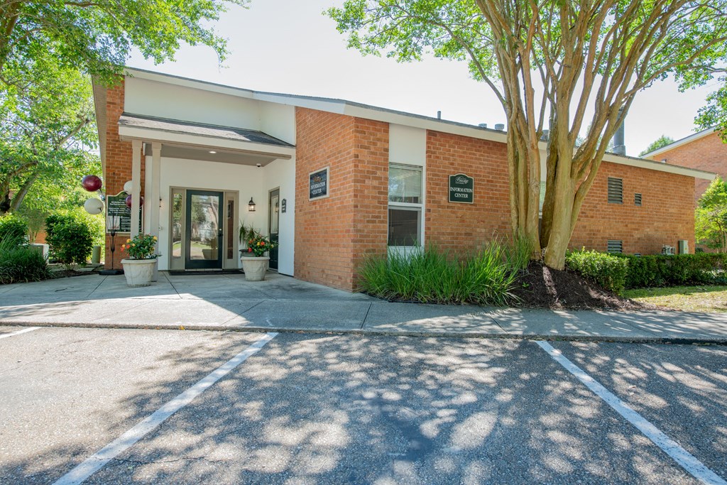 the front of a brick building with a driveway and a tree