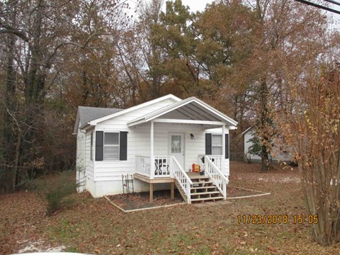 a small white house with a porch in the woods
