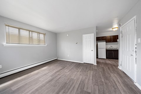 the living room and kitchen of an apartment with white walls and wood flooring