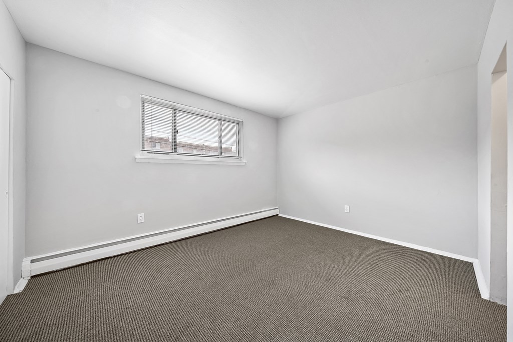 the living room of an apartment with carpet and a window