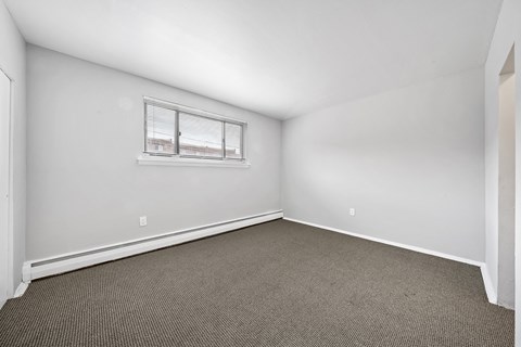 the living room of an apartment with carpet and a window