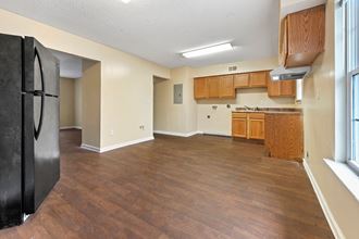 an empty living room and kitchen with wood flooring and a refrigerator
