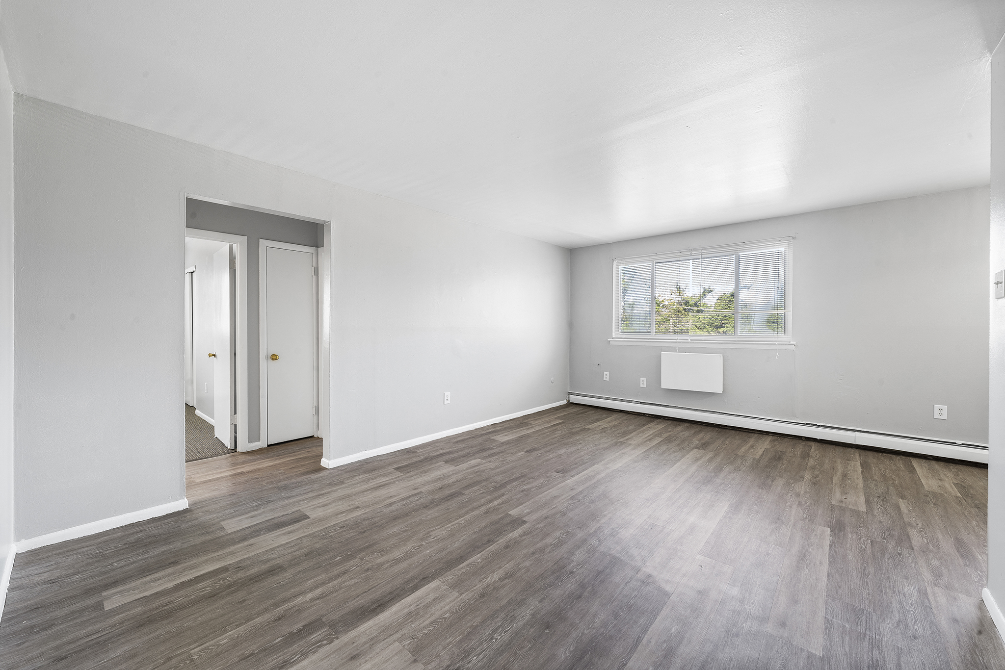 the living room of an apartment with white walls and wood floors