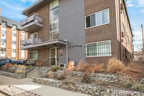 A modern brick building with a balcony and a stone wall in front.