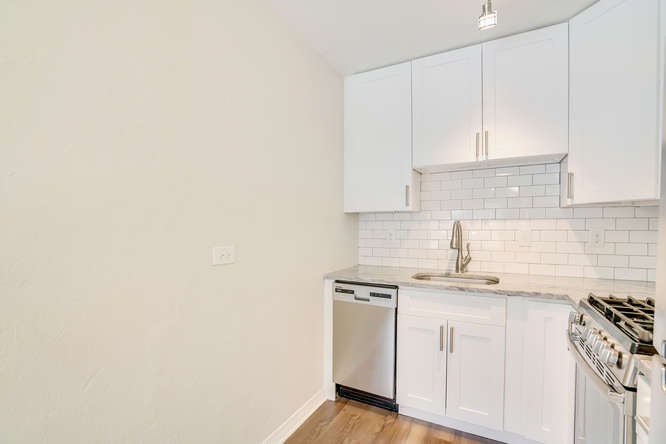 A kitchen with white cabinets and a white tiled backsplash.