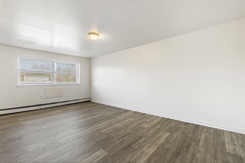 an empty room with white walls and wood flooring and a window