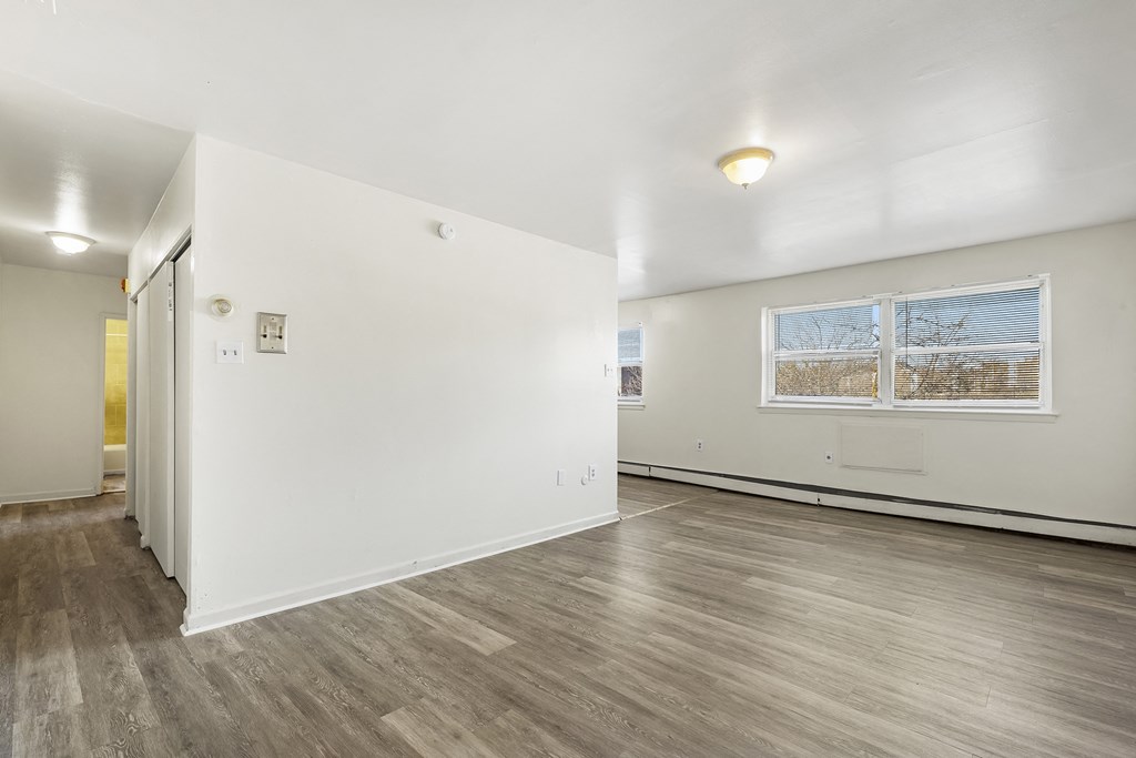 the living room and dining room of an apartment with white walls and wood floors