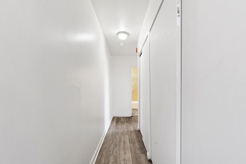 a hallway with white walls and wood floors and a white closet with a white door