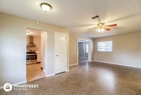 an empty living room with a ceiling fan and a kitchen