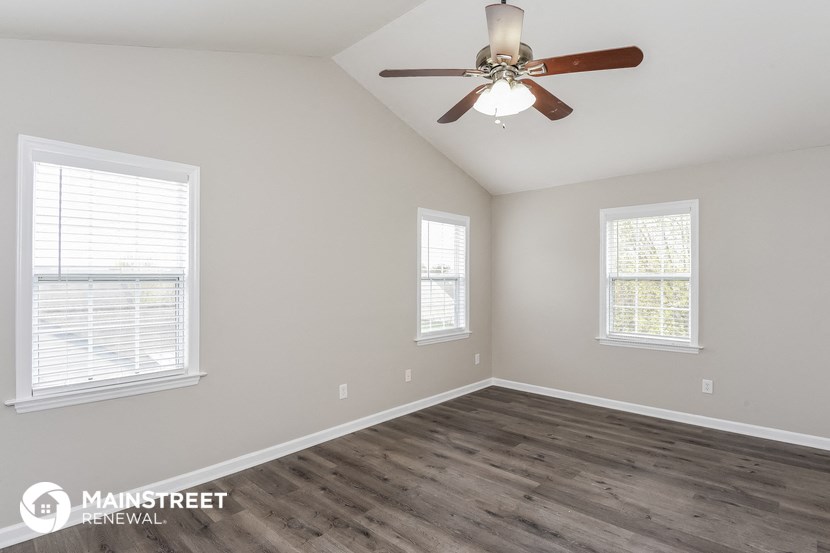 the spacious living room with wood flooring and a ceiling fan