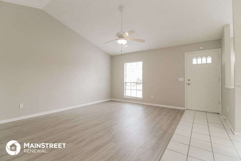 a spacious living room with white walls and a ceiling fan