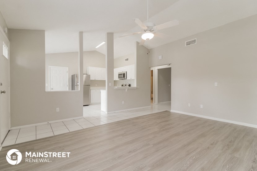 an empty living room with a ceiling fan and a kitchen