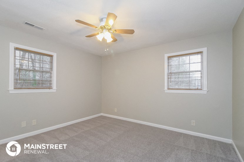 the spacious living room with ceiling fan and two windows