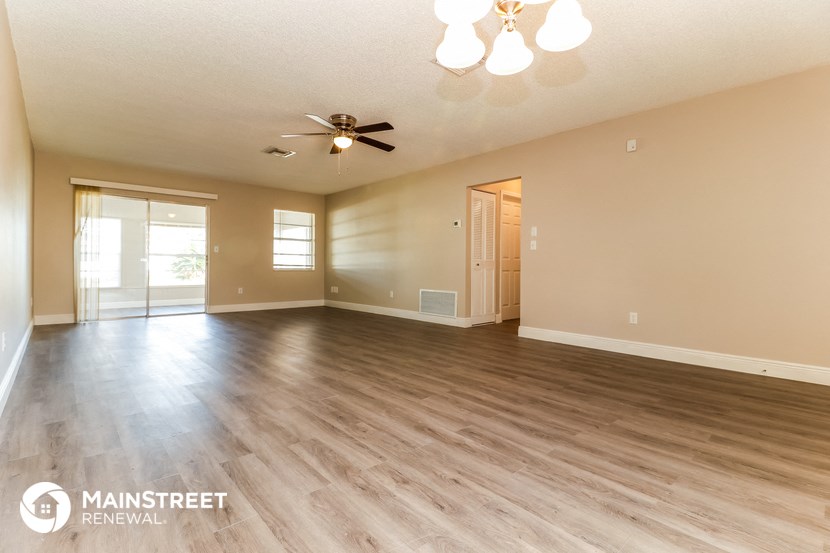 the spacious living room with hardwood flooring and a ceiling fan