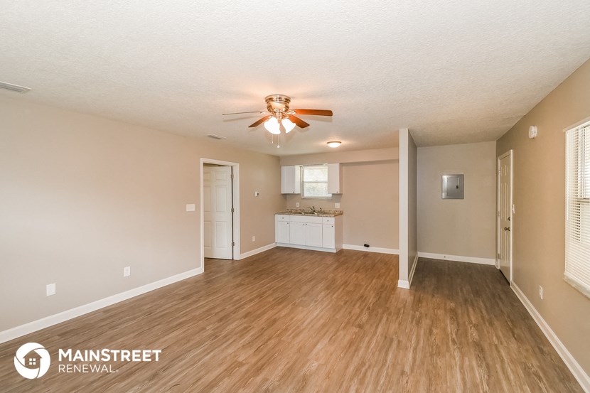 an empty living room with a ceiling fan and a kitchen