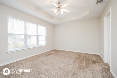 the spacious living room of a new home with carpet and a ceiling fan