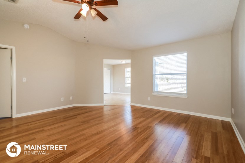 the spacious living room with hardwood flooring and a ceiling fan