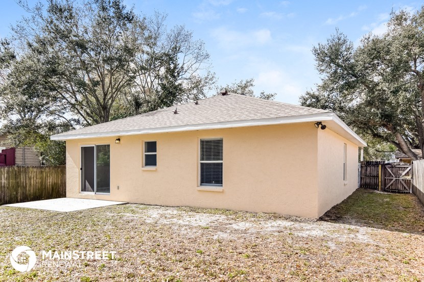 the backyard of a small tan house with a yard and trees