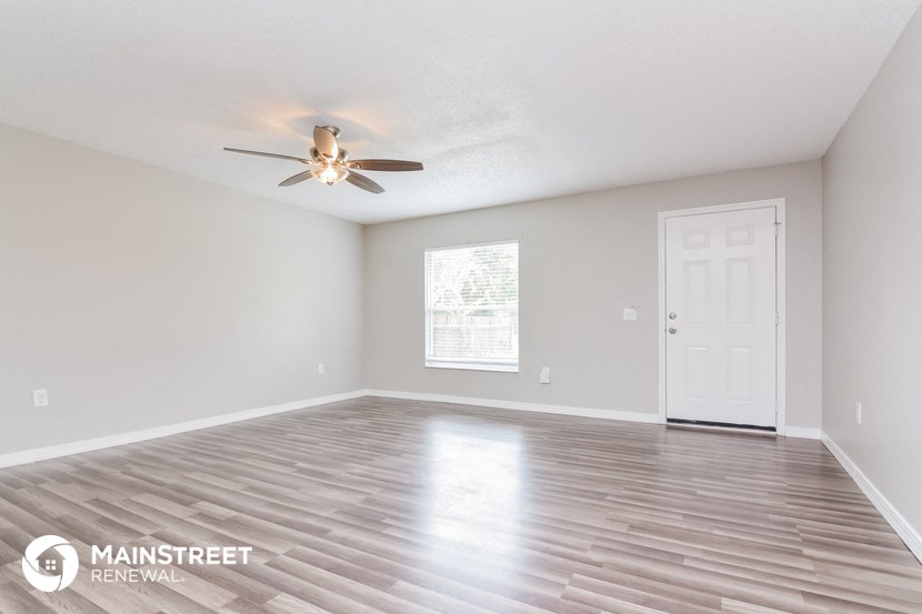 the spacious living room with wood floors and a ceiling fan