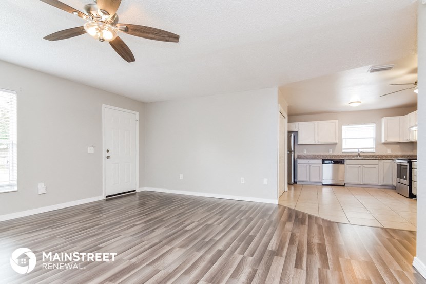 an empty living room with a ceiling fan and a kitchen