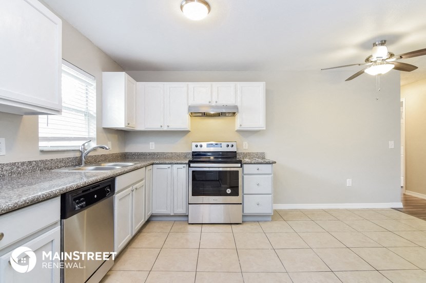 a kitchen with white cabinets and a sink and a stove and a ceiling fan