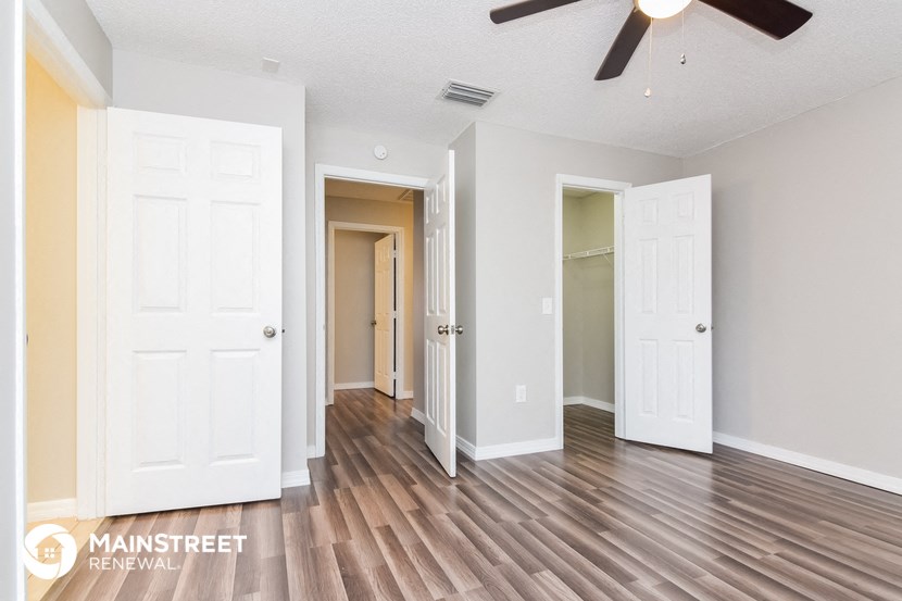 the living room and hallway of an apartment with wood flooring and a ceiling fan