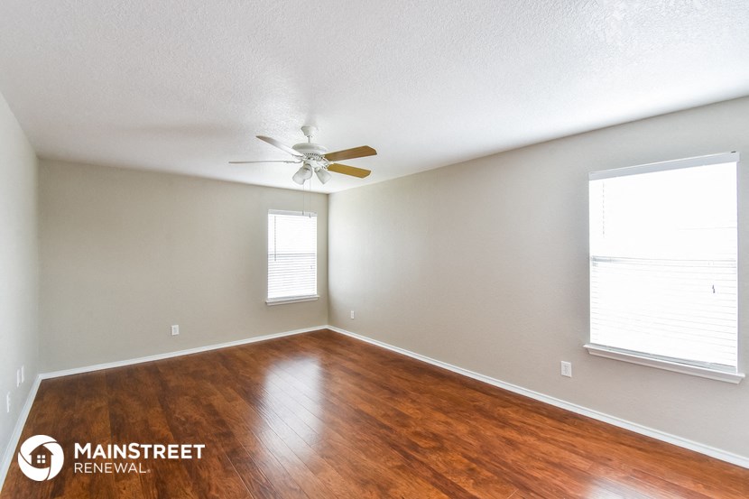 the spacious living room with hardwood flooring and ceiling fan