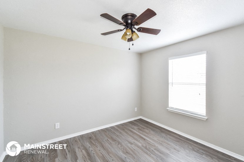 the spacious living room with a ceiling fan and a window