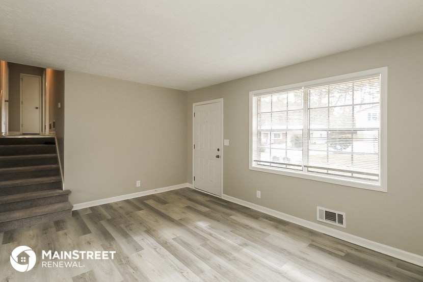 the living room of an apartment with wood flooring and a large window