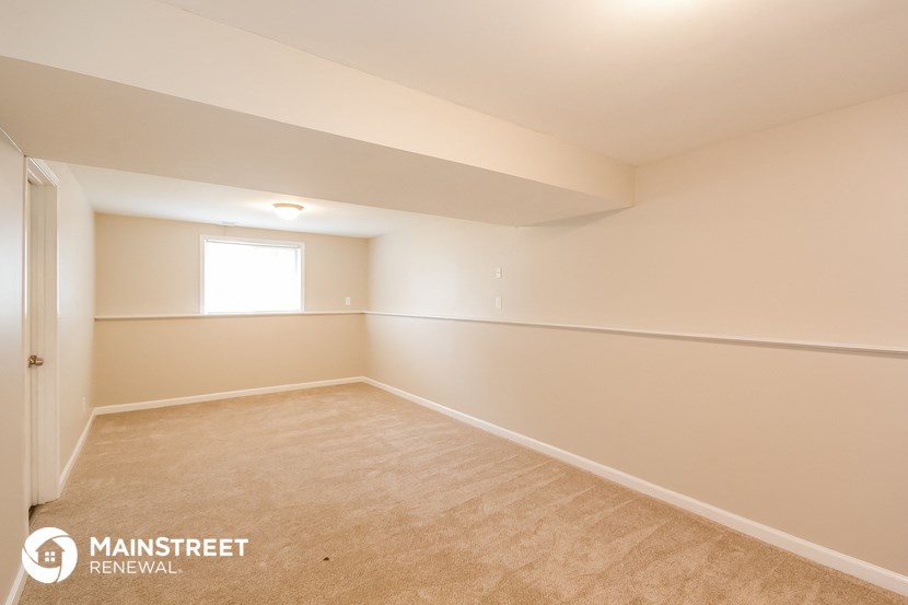 the upstairs bedroom of an apartment with beige carpet and a window