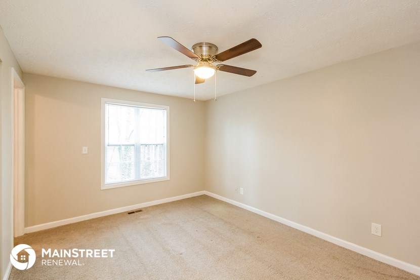 the spacious living room with ceiling fan and carpeting