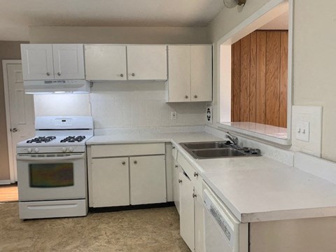 A white kitchen with a stove, sink, and cabinets.