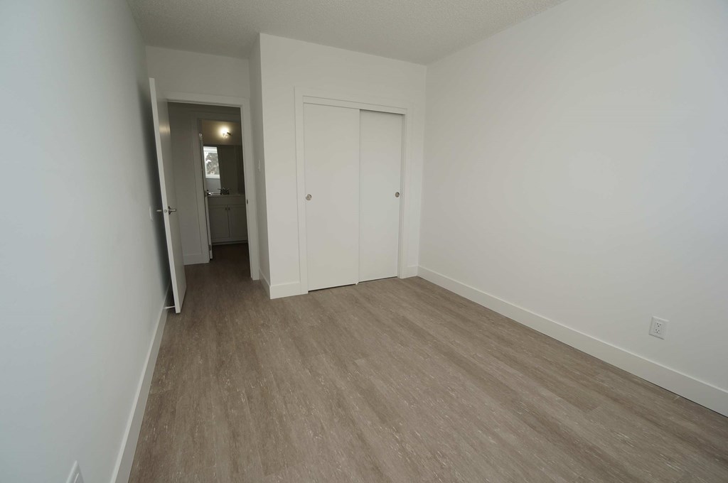 a bedroom with white walls and wood flooring and a closet