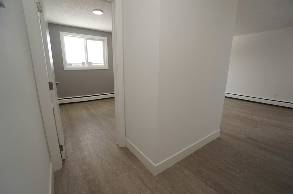 a bedroom with white walls and wood flooring and a window
