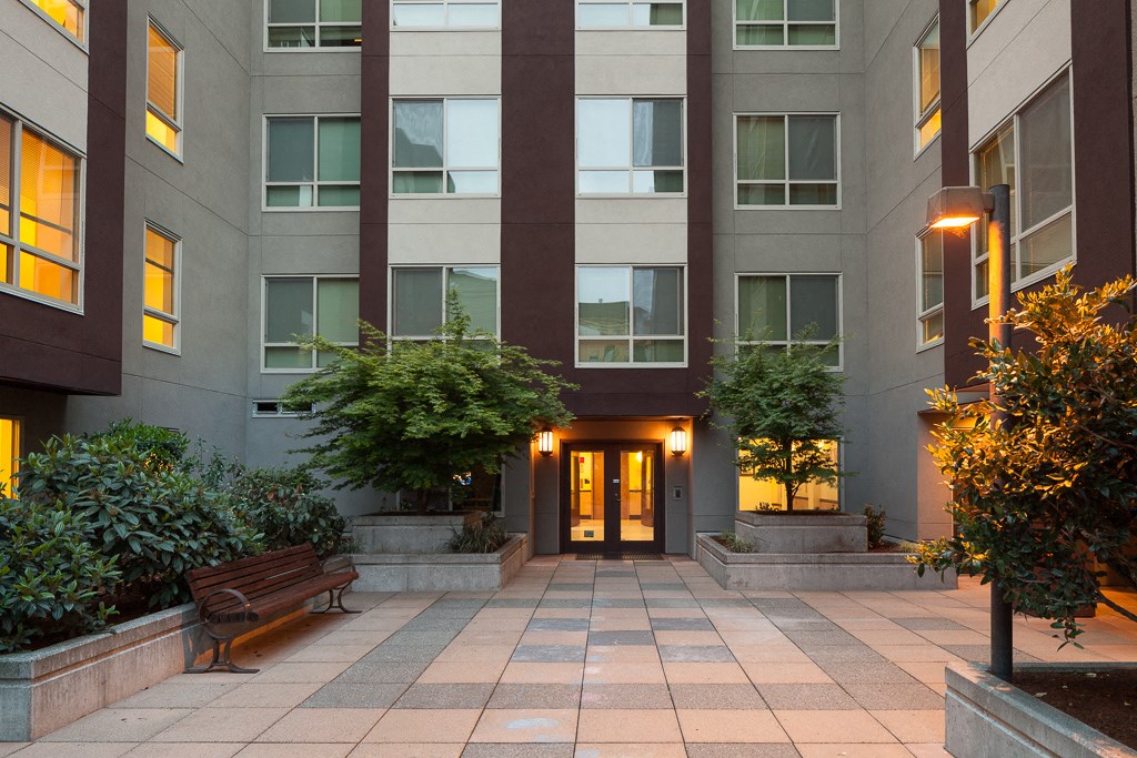 the entrance to an apartment building with benches and plants