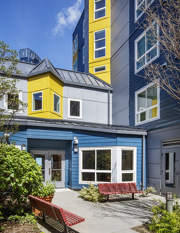a blue house with a yellow and white addition and a courtyard with benches
