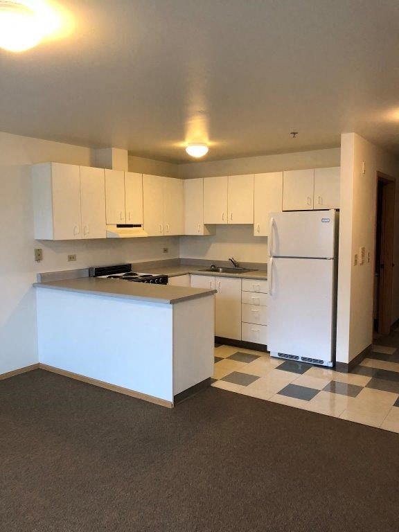an empty kitchen with white cabinets and a refrigerator