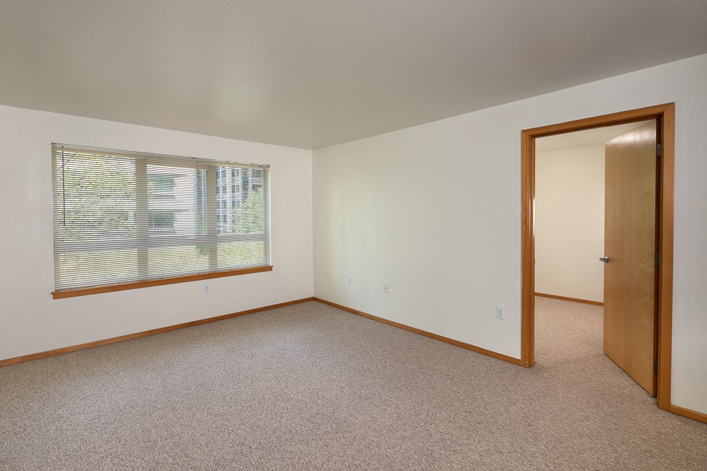 A room with a carpeted floor, a window with blinds, and a door.