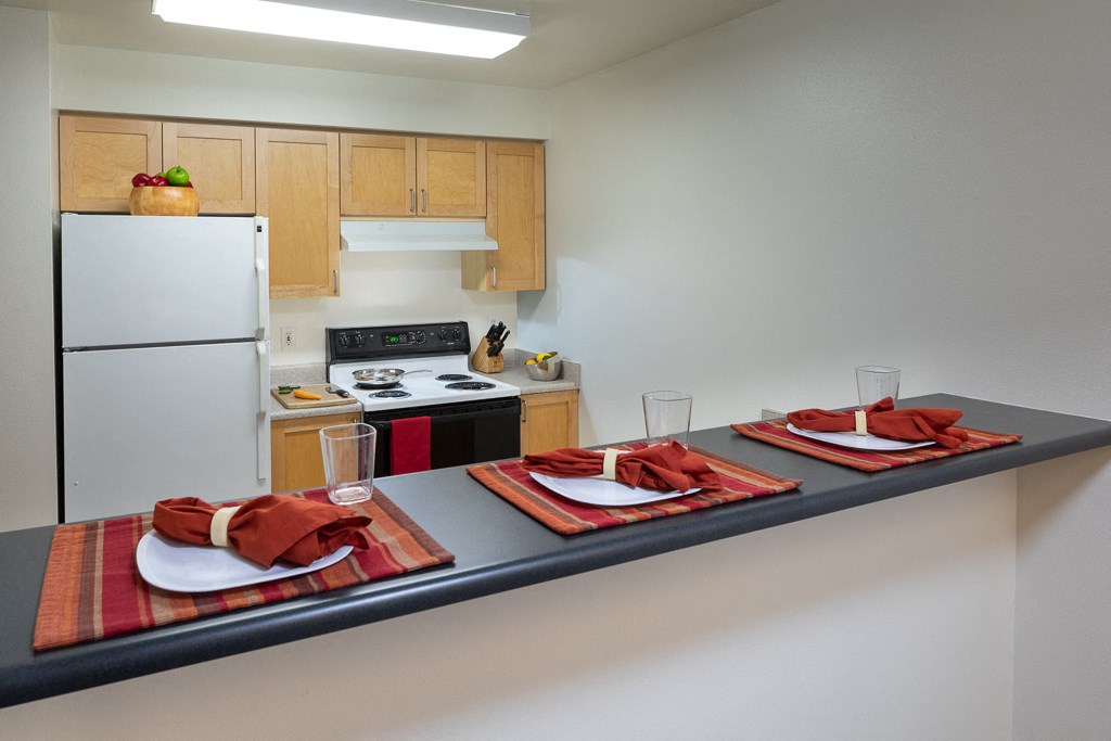 A kitchen with a refrigerator, stove, and a table set for two.