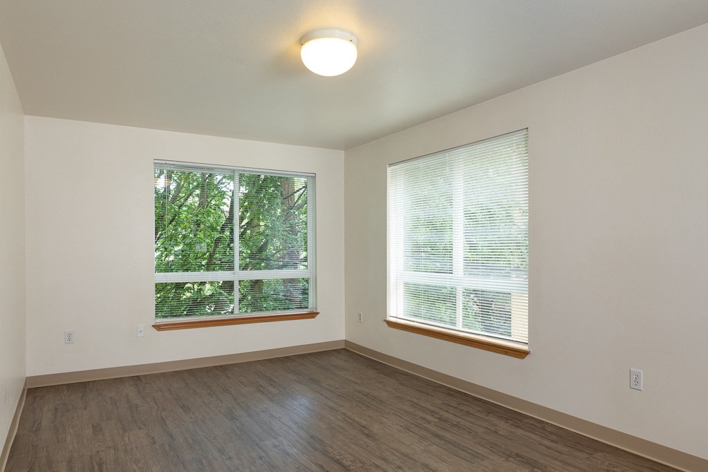 an empty living room with two windows and wood flooring