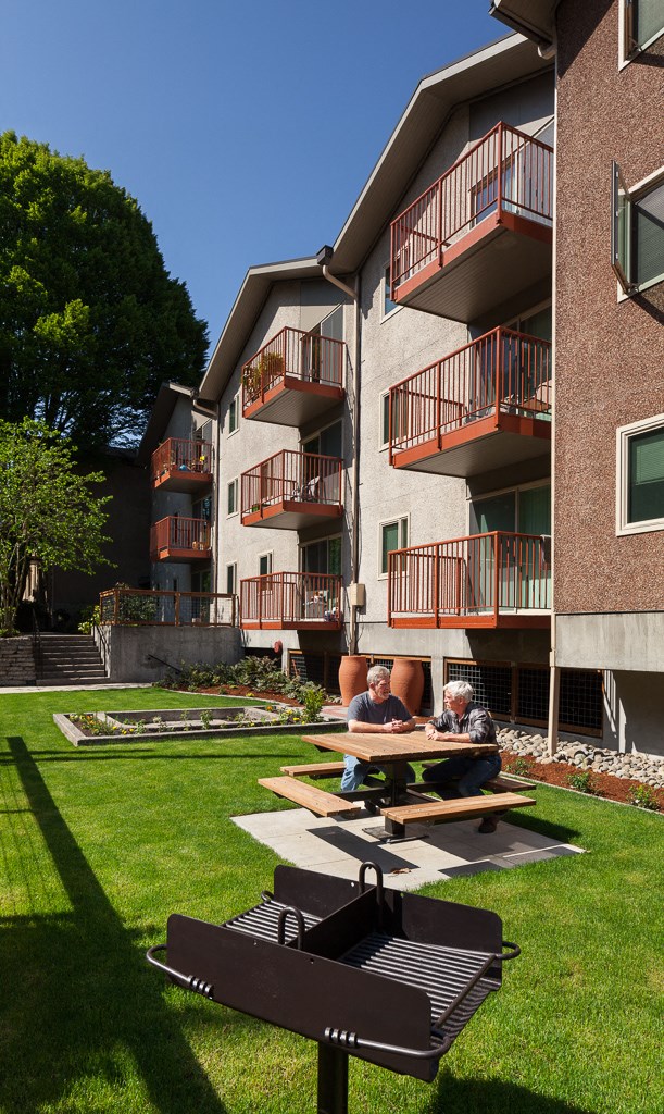 two people sit on a picnic table outside of an apartment building